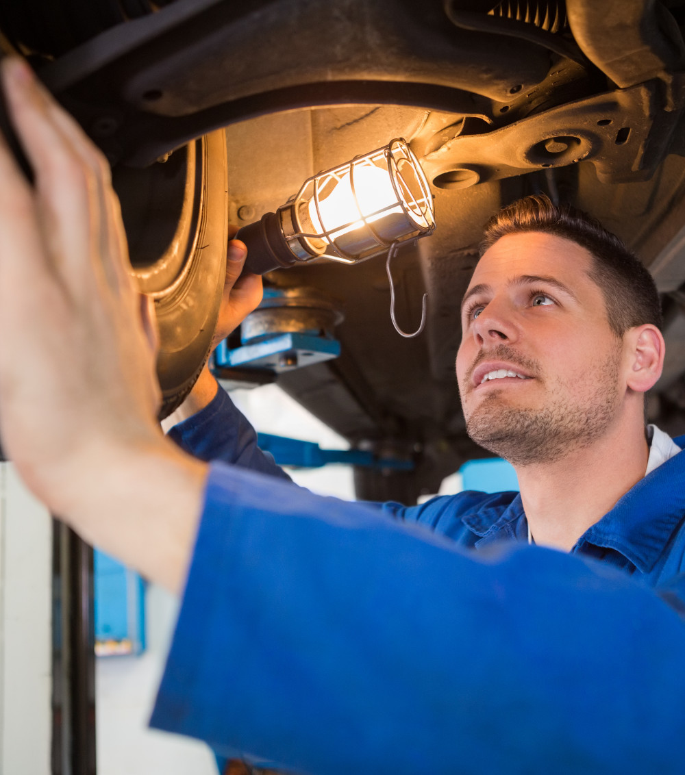 Mechanic using torch to look under car at the repair garage - MOT Testing Batley